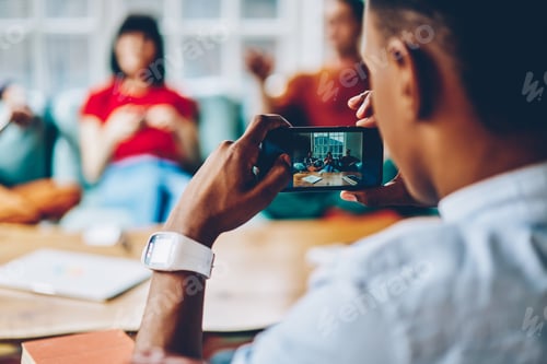 Preview: Ethnic man shooting with smartphone friends while resting together at home