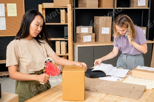 Preview: Young Asian woman sealing packed order in cardboard box against colleague