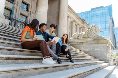 Preview: Students collaborating on university campus steps using digital tablet