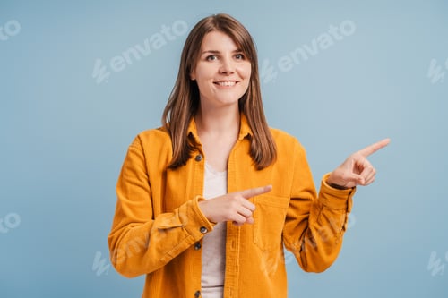 Preview: Beautiful, smiling middle aged woman wearing yellow shirt, pointing with fingers at space