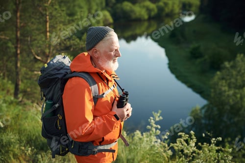 Preview: Mature Tourist In Orange Jacket At Bank Of River