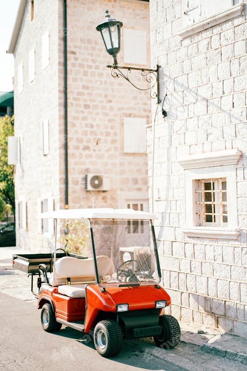 Preview: Red golf car with a trailer stands near an old stone house on the street