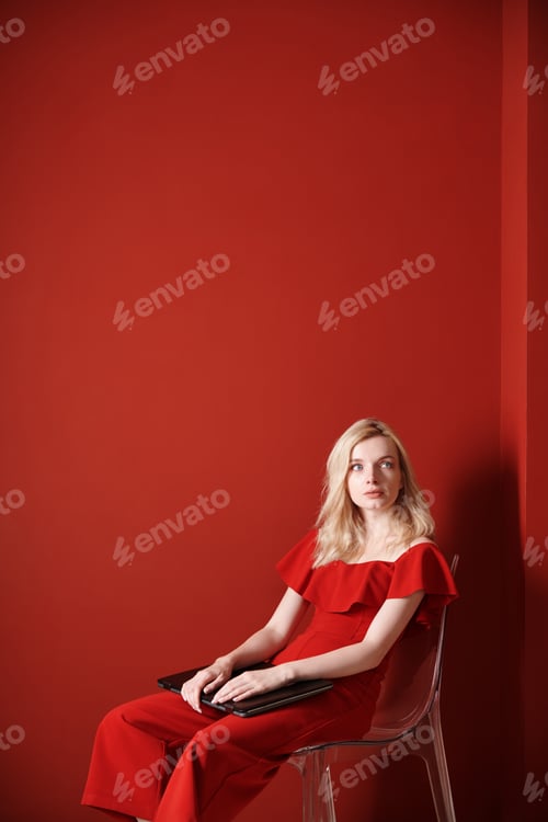 Preview: Young adult woman sitting on a chair and holding laptop