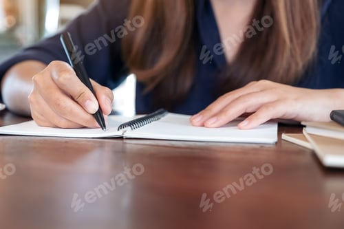 Preview: Closeup image of avwoman writing on blank notebook on table in cafe