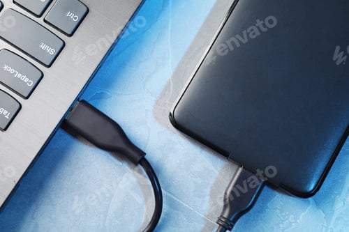 Preview: Hard disk drive with USB cable connected to laptop on blue textured table, top view