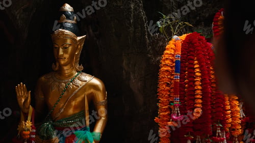 Preview: Golden statue depicting buddha or a deity with traditional flower garlands in a temple cave