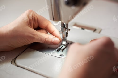 Preview: Beginning of sewing process. Woman's hands pulling loop threads through the presser foot.