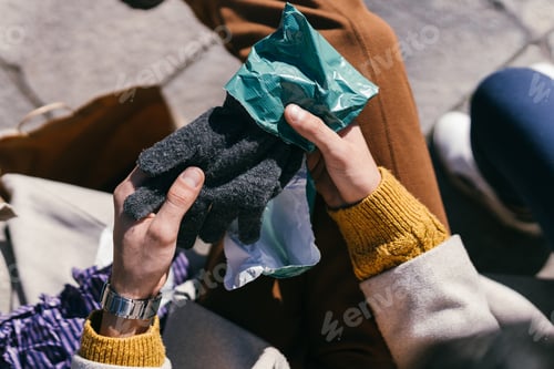 Preview: Man holding a pair of woolen gloves he has just been given sitting on a bench