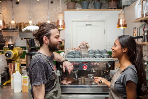 Preview: Male and female baristas talking by cafe coffee machine