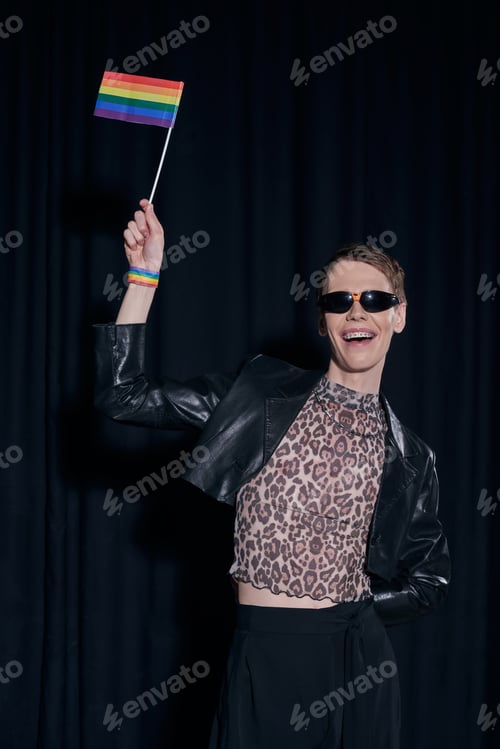 Preview: Cheerful and fashionable nonbinary person in leather jacket and top with animal print holding lgbt