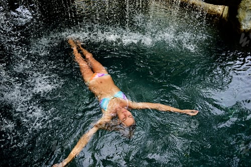 Preview: Young woman floating in water in pool with waterfall