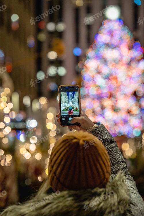 Preview: Female using her mobile device to take a photograph of a Christmas tree in the background
