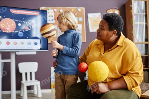 Preview: Mature teacher of nursery school and little schoolboy with planet models