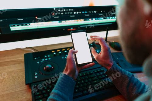 Preview: Male Video Editor sitting at his Computer using phone blank screen