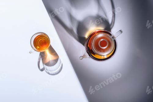 Preview: top view of healthy herbal tea in glass cup and kettle with shadows on grey
