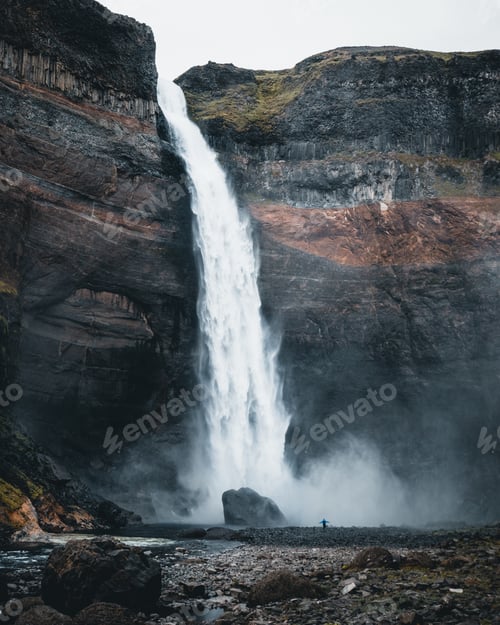 Preview: Lonely person enjoying the beautiful view of the waterfall surrounded by rocky cliffs in Iceland