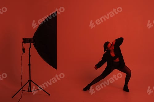 Preview: confident girl is photographed in black tights, jacket, bathed in red light