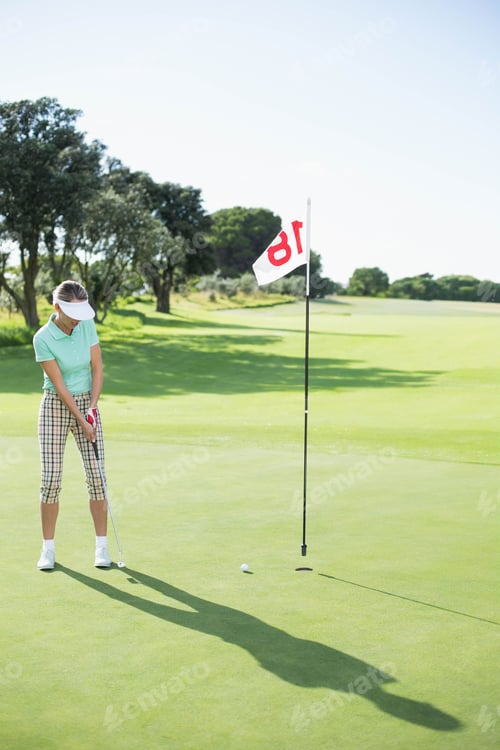 Aperçu: Senior golfer in golf attire aligning putter with ball on putting green hole 18, copy space