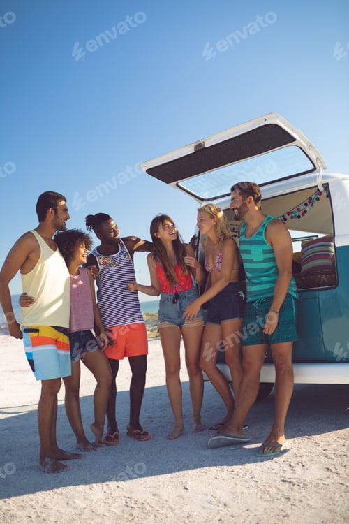 Preview: Front view of happy group of diverse friends interacting with each other near camper van at beach