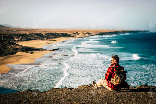 Preview: Wanderlust and travel people concept with hipster man sitting on the rocks at the cliff