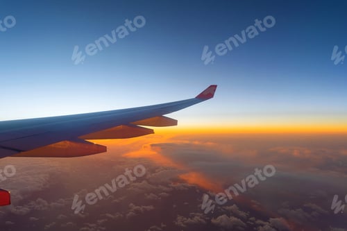 Preview: Wing of an airplane jet flying above clouds with blue sky from the window in travel concept