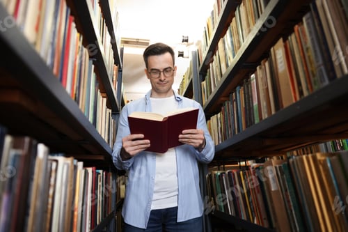 Preview: Man reading book near shelves in public library, low angle view