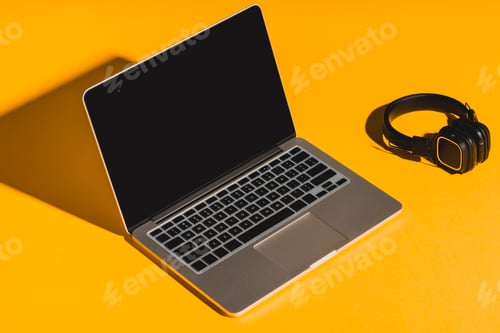 Preview: headphones and laptop with blank screen on yellow background