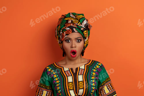 Preview: Shocked african woman in traditional clothing grimacing on orange