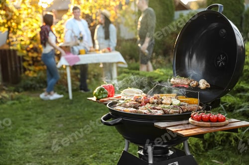 Preview: Group of friends having party outdoors. Focus on barbecue grill with food. Space for text