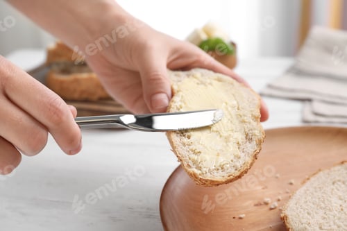 Preview: Woman spreading butter on slice of bread over table, closeup