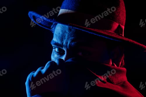 Preview: Young handsome model posing in a studio in a trendy neon light in a stylish suit and hat