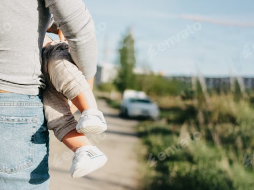 Preview: Young woman mother holding her baby on hands outdoors