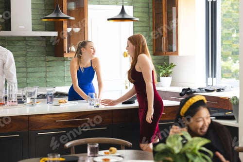 Preview: Teen girls in elegant dresses laughing together in modern kitchen during celebration