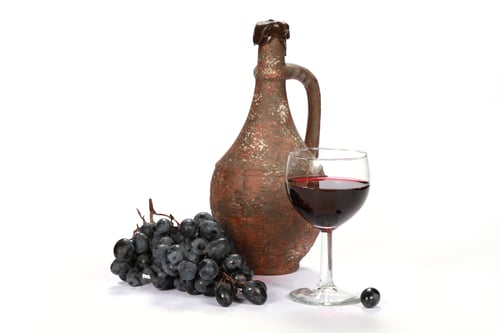 Preview: Glass of wine, an ancient pitcher, and some grapes on a white surface