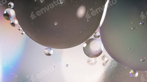 Preview: Oil circles close-up in water on glass surface under light lighting