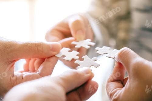 Preview: Closeup image of many people holding and putting a piece of white jigsaw puzzle together