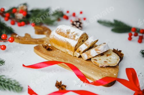 Preview: Sweet bread with powdered sugar sliced on wooden board with red ribbon and pine