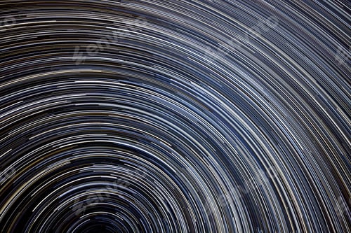 Preview: Star trails in the night sky with sweeping curves of white and blue against a dark background
