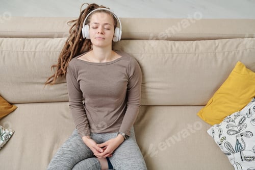 Preview: Peaceful young woman with headphones listening to meditation music on couch