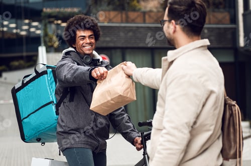 Preview: Male courier with bicycle delivering fast food to the customer in city.
