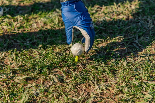 Preview: closeup of senior golfer's hand placing golf ball on tee wearing blue glove