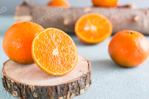 Preview: Ripe tangerine cut in half on a tree saw cut and tangerines nearby on a blue background.