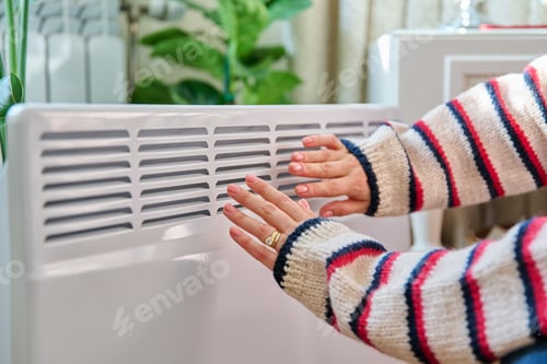Preview: Close-up of woman hands warming near electric heating radiator