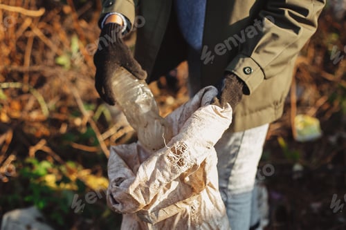 Preview: Woman hand in glove picking up trash, collecting garbage in bag