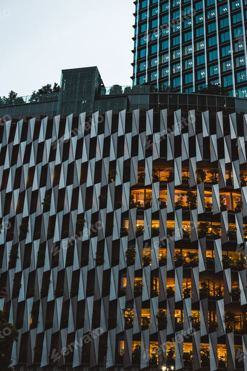 Preview: Modern building facade with unique geometric patterns and illuminated interiors at dusk