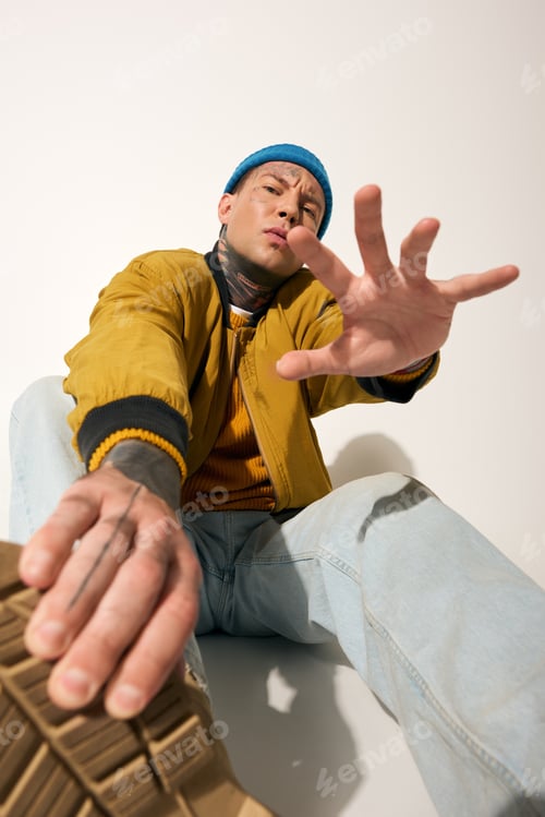 Preview: Young man with tattoos striking a pose in a stylish urban outfit in a bright studio setting