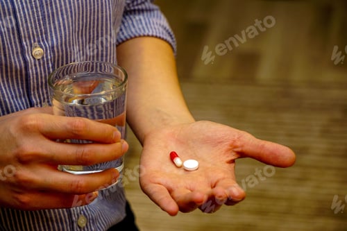 Preview: Closeup of capsules and a glass of water in woman's hands