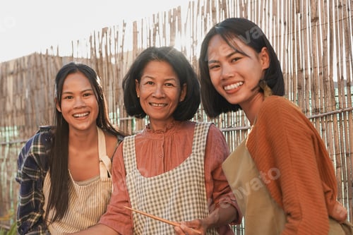 Preview: Happy asian mother and adult daughters miling on camera while cooking traditional thai food