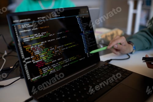 Preview: Focus on laptop screen with coded data and pen held by hand of young man