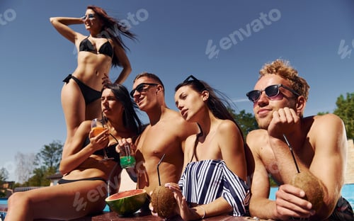 Preview: Sunny warm weather. Group of young happy people have fun in swimming pool at daytime